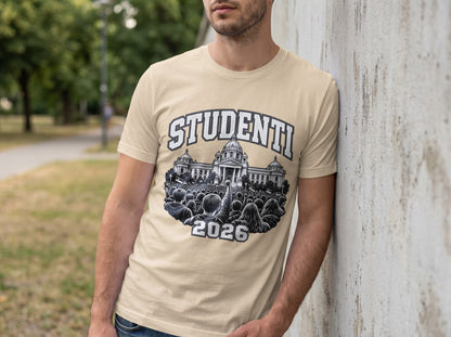 A man leaning against a concrete wall wearing a beige crewneck t-shirt featuring a black and white graphic with the text "STUDENTI 2026".