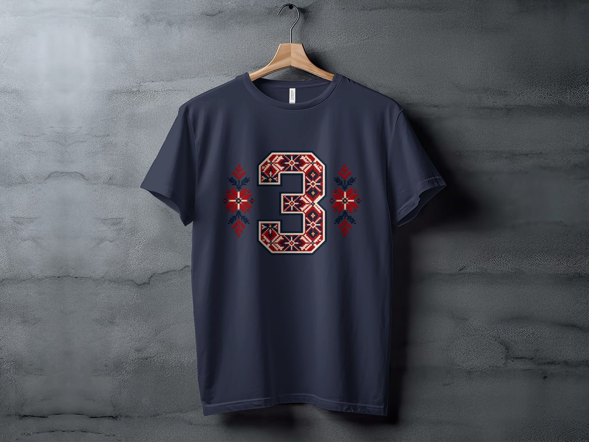 A dark blue t-shirt hanging on a wooden hanger features a large, red and white Nordic-style number three graphic with matching snowflake accents.