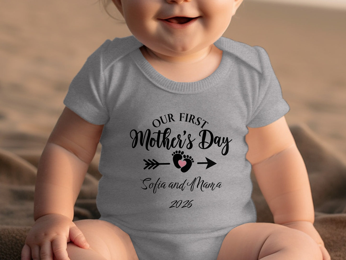 Baby wearing a grey onesie with "Our First Mother's Day" text and footprints.