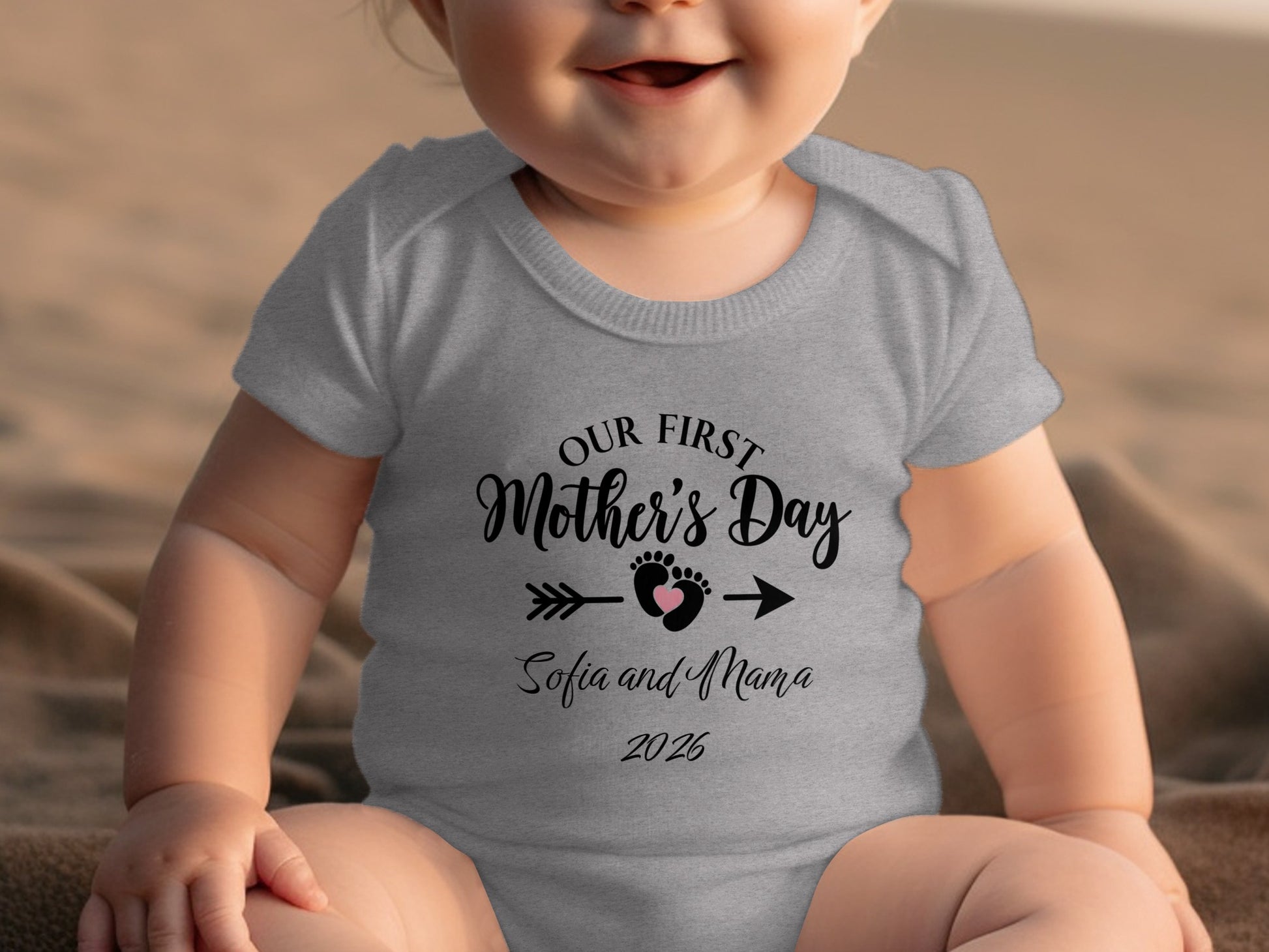 Baby wearing a grey onesie with "Our First Mother's Day" text and footprints.