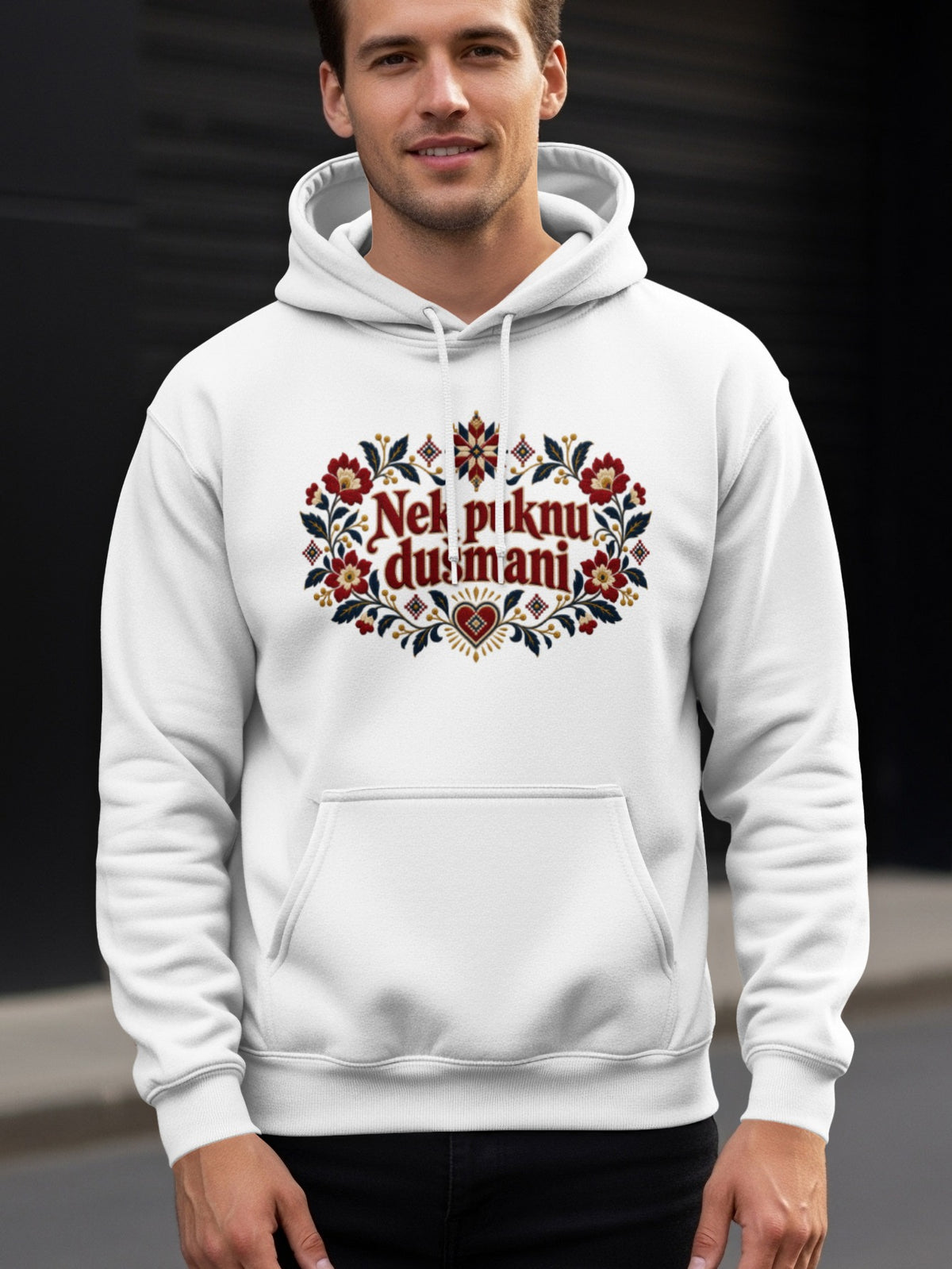 A smiling man wearing a white hooded sweatshirt with a decorative floral chest print.