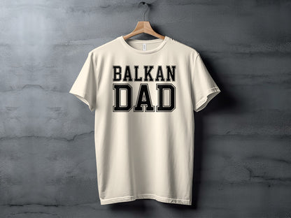 Cream t-shirt with bold black text "BALKAN DAD" hanging on a hanger.