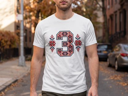 A man wearing a white t-shirt with a blue, red, and white Nordic-style number three graphic on the chest.