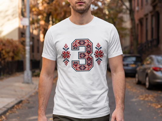 A man wearing a white t-shirt with a blue, red, and white Nordic-style number three graphic on the chest.