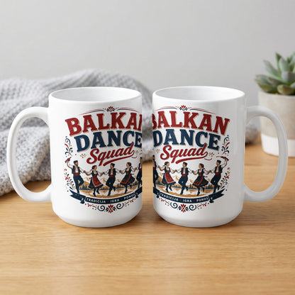 Two white mugs with "Balkan Dance Squad" text and traditional dancers on a wooden table.