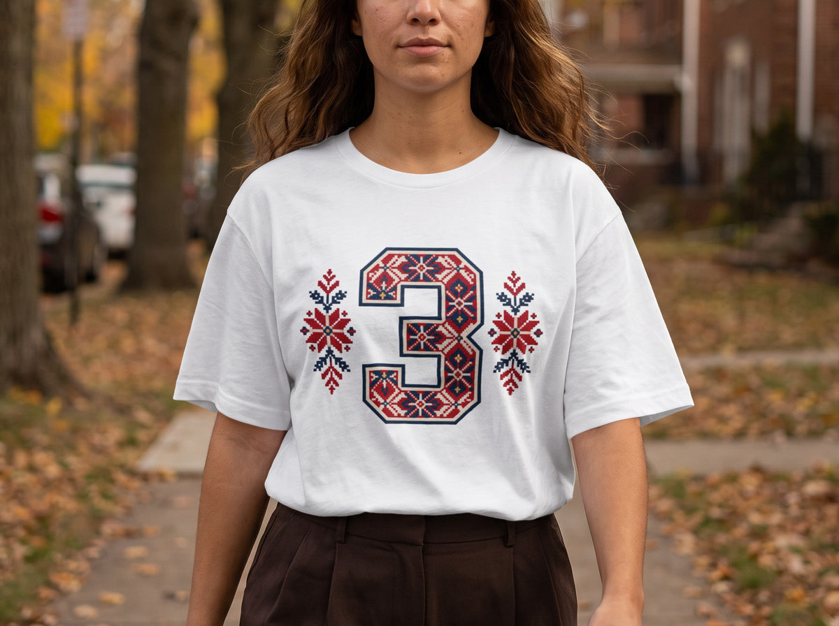A person wearing a white t-shirt featuring a large number three with red and blue Nordic-style patterns.