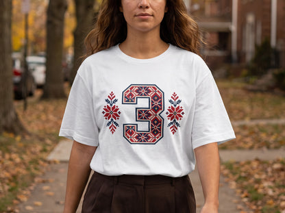 A person wearing a white t-shirt featuring a large number three with red and blue Nordic-style patterns.