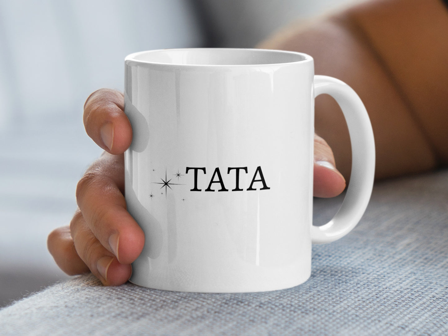 White mug with black text "TATA" and star graphic held by a hand.
