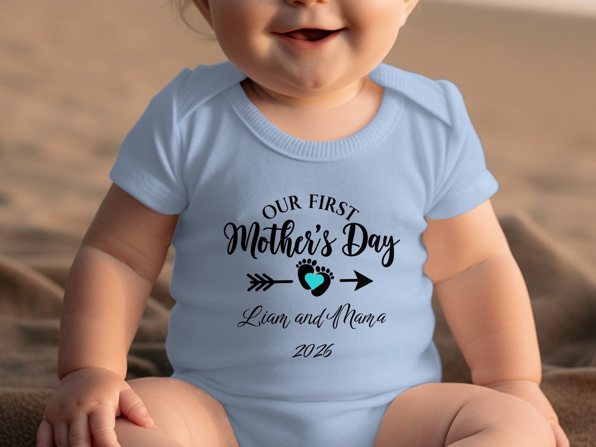 Light blue baby onesie with "Our First Mother's Day" text and heart.