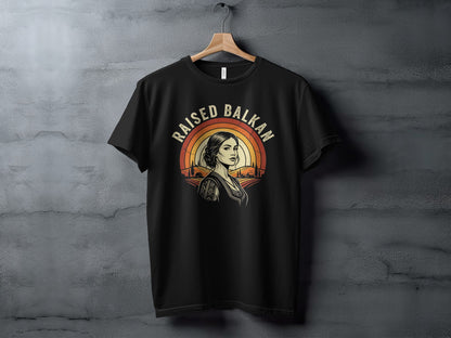Black t-shirt with "Raised Balkan" text and a woman's profile against a sunset.