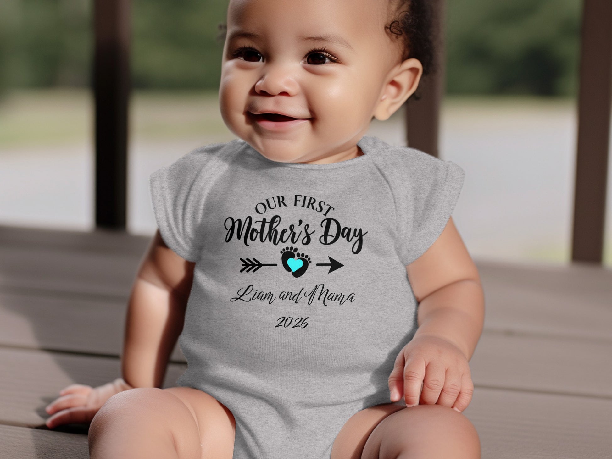 Baby in gray bodysuit reading "Our First Mother's Day" with baby's name and year.