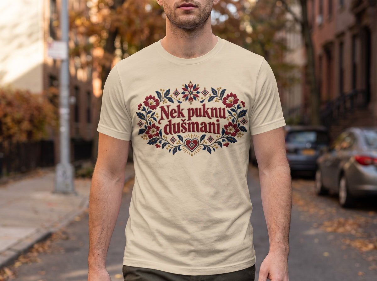 A man wearing a cream t-shirt featuring a colorful floral motif and the text Nek puknu dušmani.
