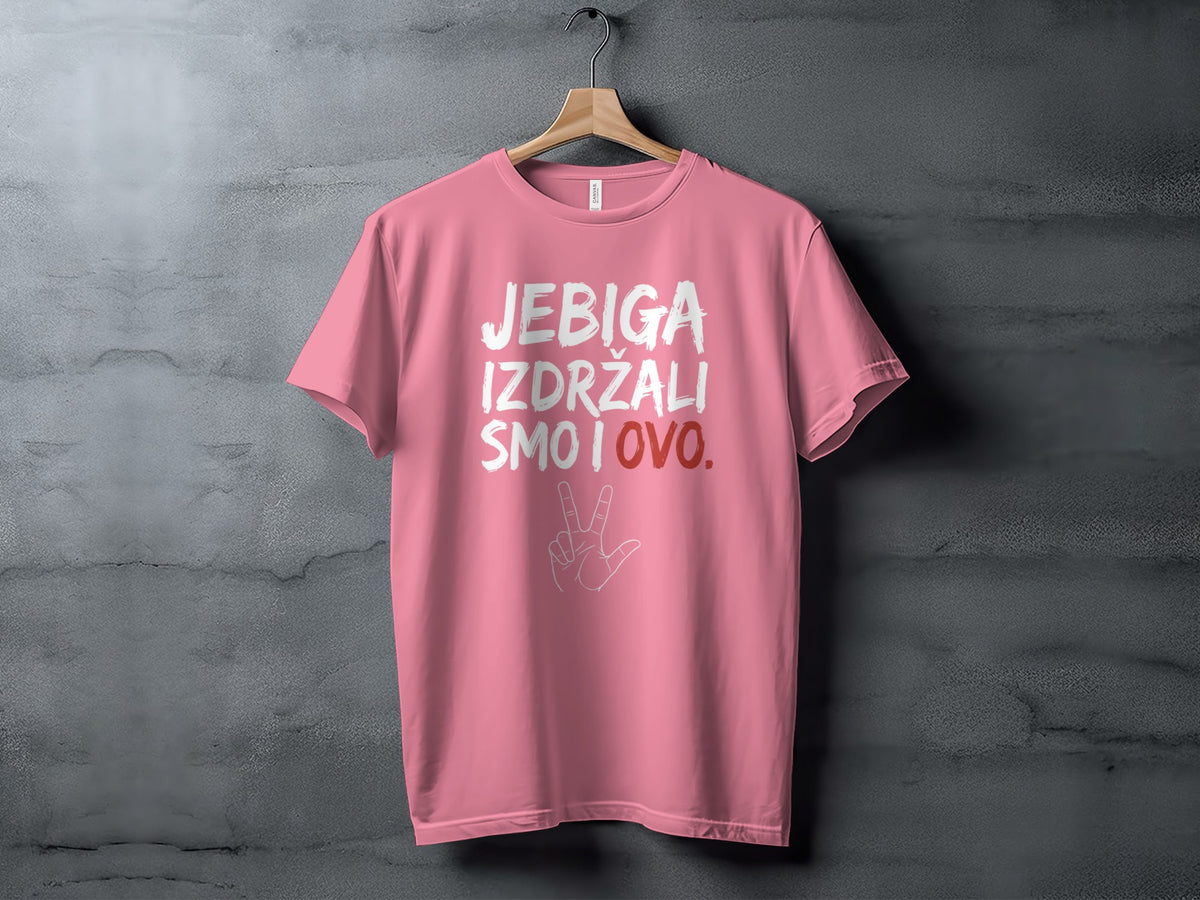 A pink short-sleeved t-shirt hangs on a wooden hanger against a gray textured wall, featuring white and red printed text.