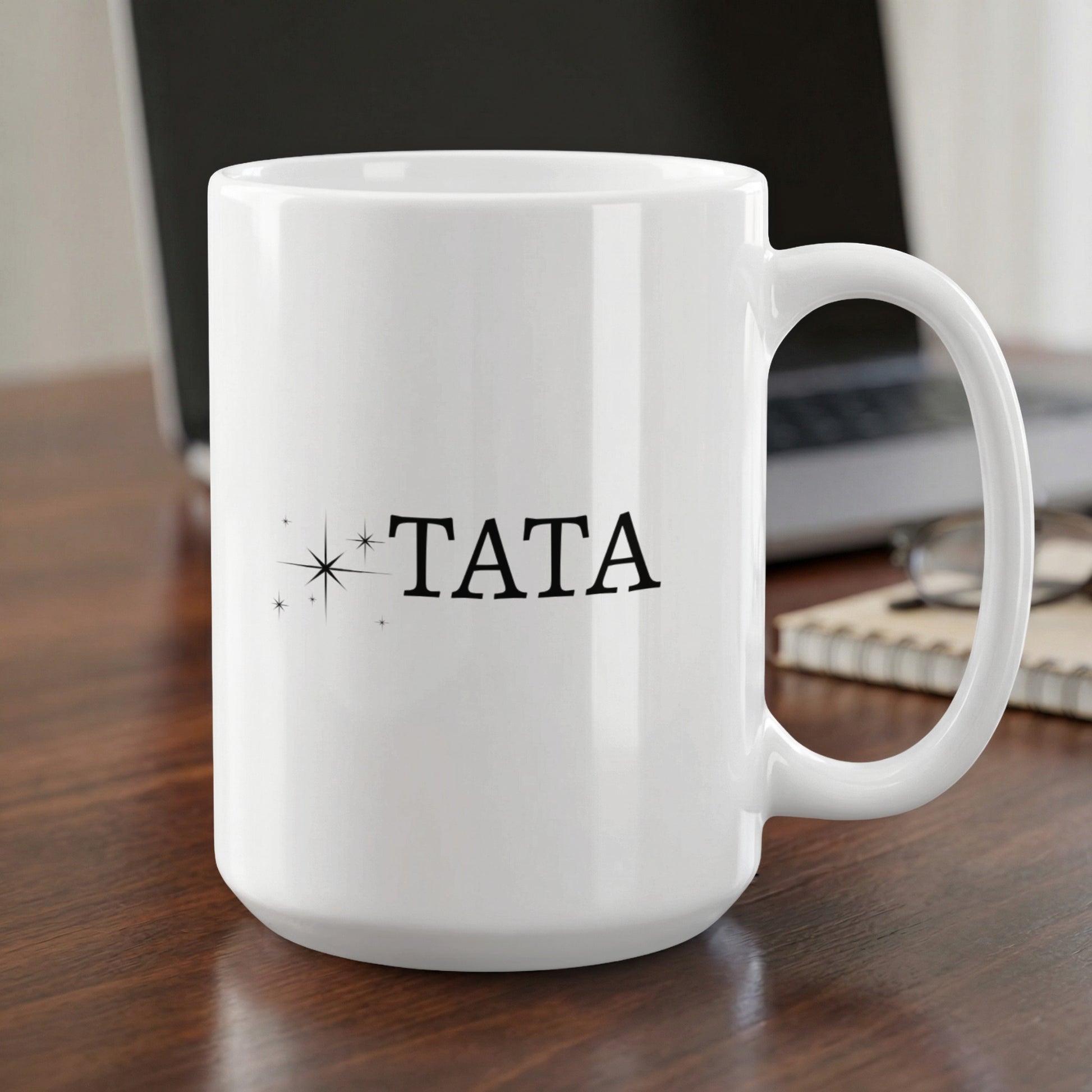 White mug with "TATA" printed in black, on a wooden desk.