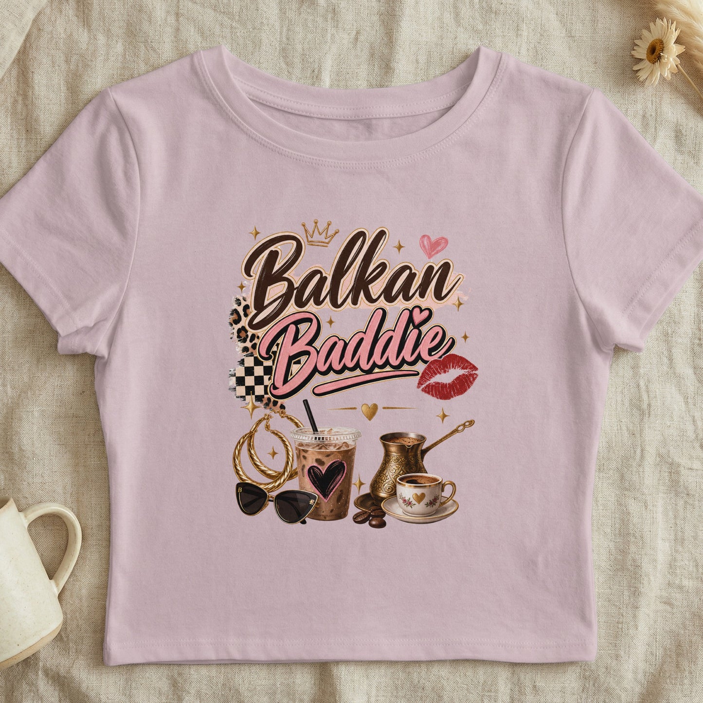 Pink t-shirt with "Balkan Baddie" text, crown, heart, lips, coffee, and accessories.