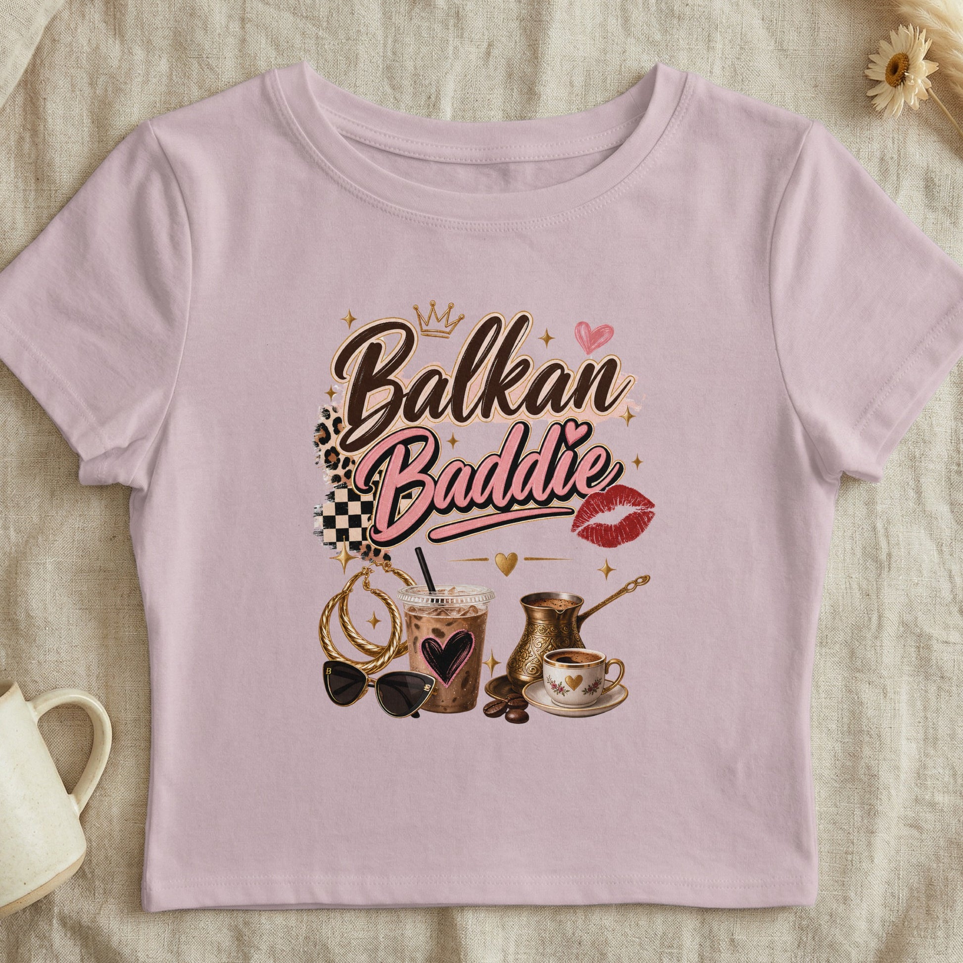 Pink t-shirt with "Balkan Baddie" text, crown, heart, lips, coffee, and accessories.