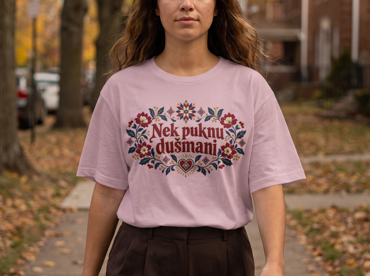A woman wearing a pink t-shirt with red and blue floral embroidery framing the text Nek puknu dušmani.
