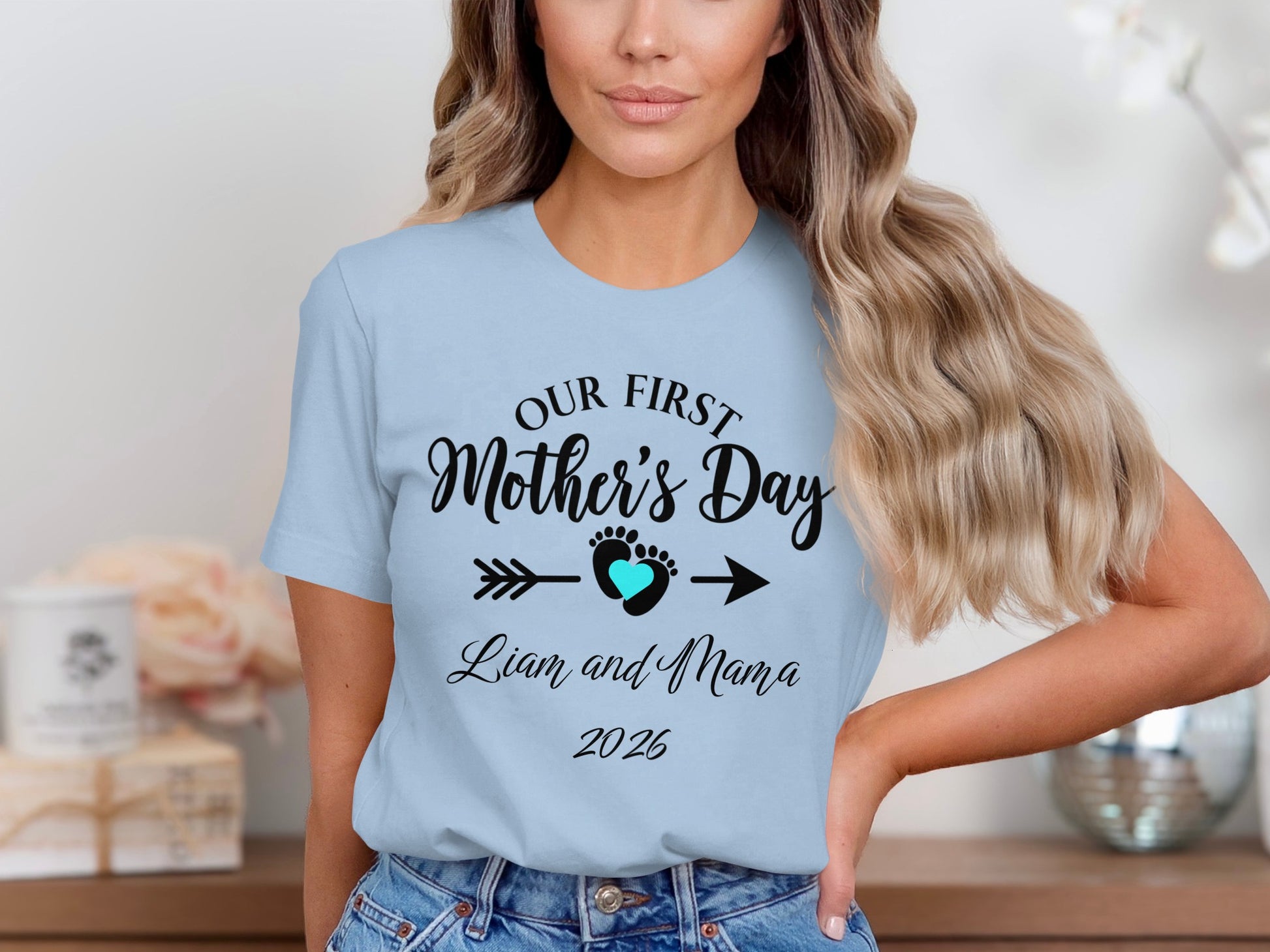 Light blue t-shirt with "Our First Mother's Day Liam and Mama 2026" text and heart arrow graphic.