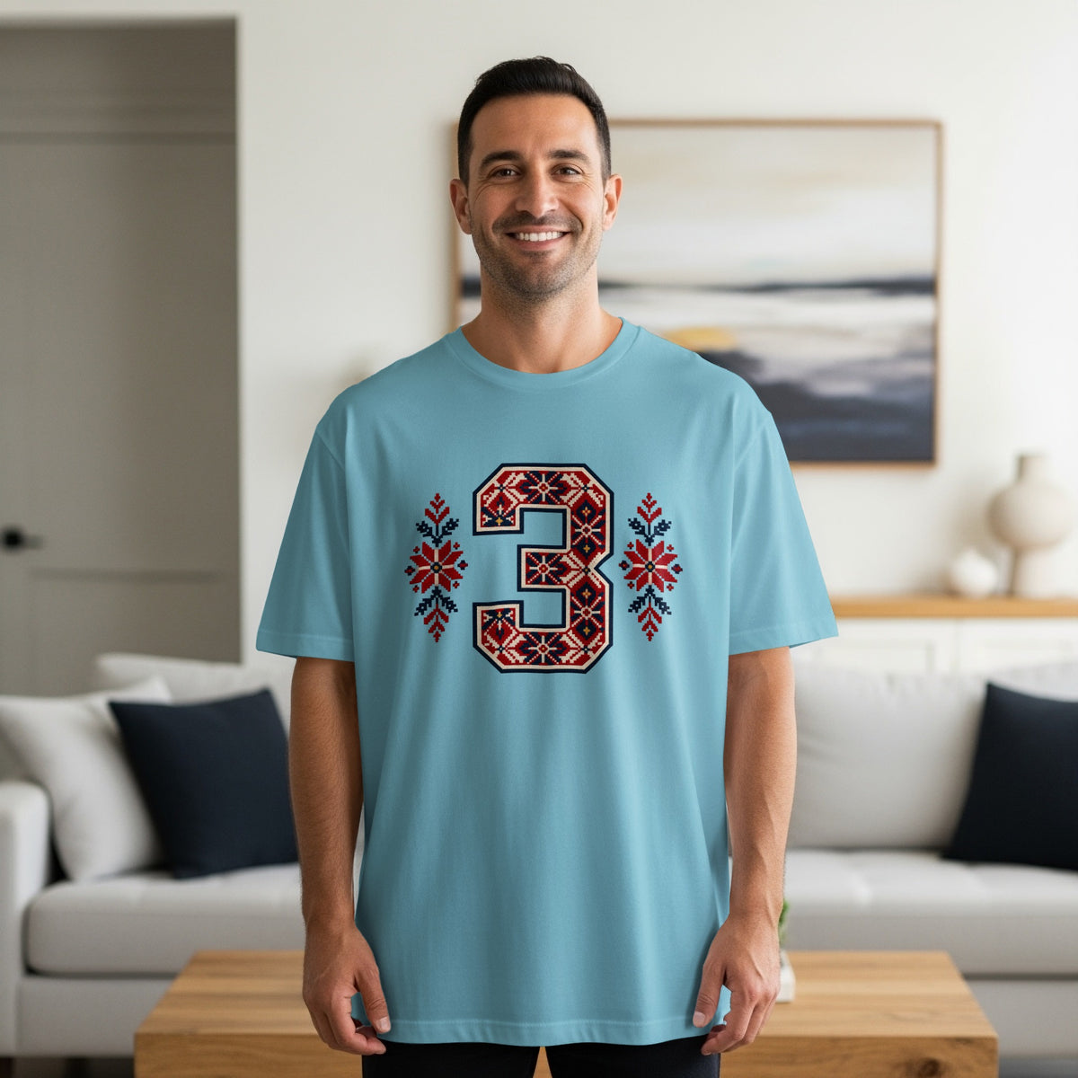 A smiling man wearing a light blue t-shirt with a red and blue Nordic-style number three graphic.