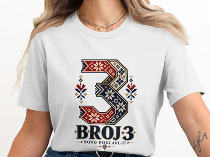 A woman wearing a white t-shirt featuring a stylized number three in traditional folk embroidery patterns.