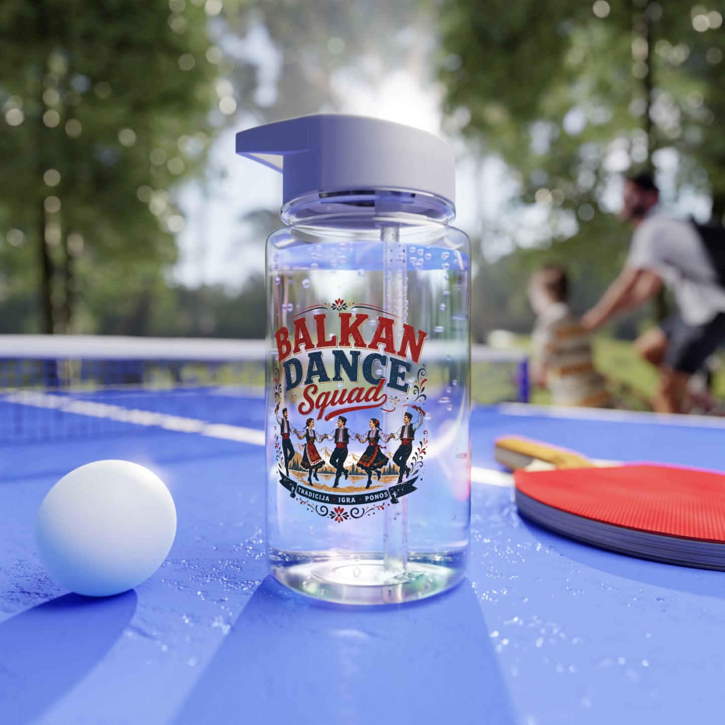 Clear bottle with "Balkan Dance Squad" label on blue ping pong table with ball and paddle.