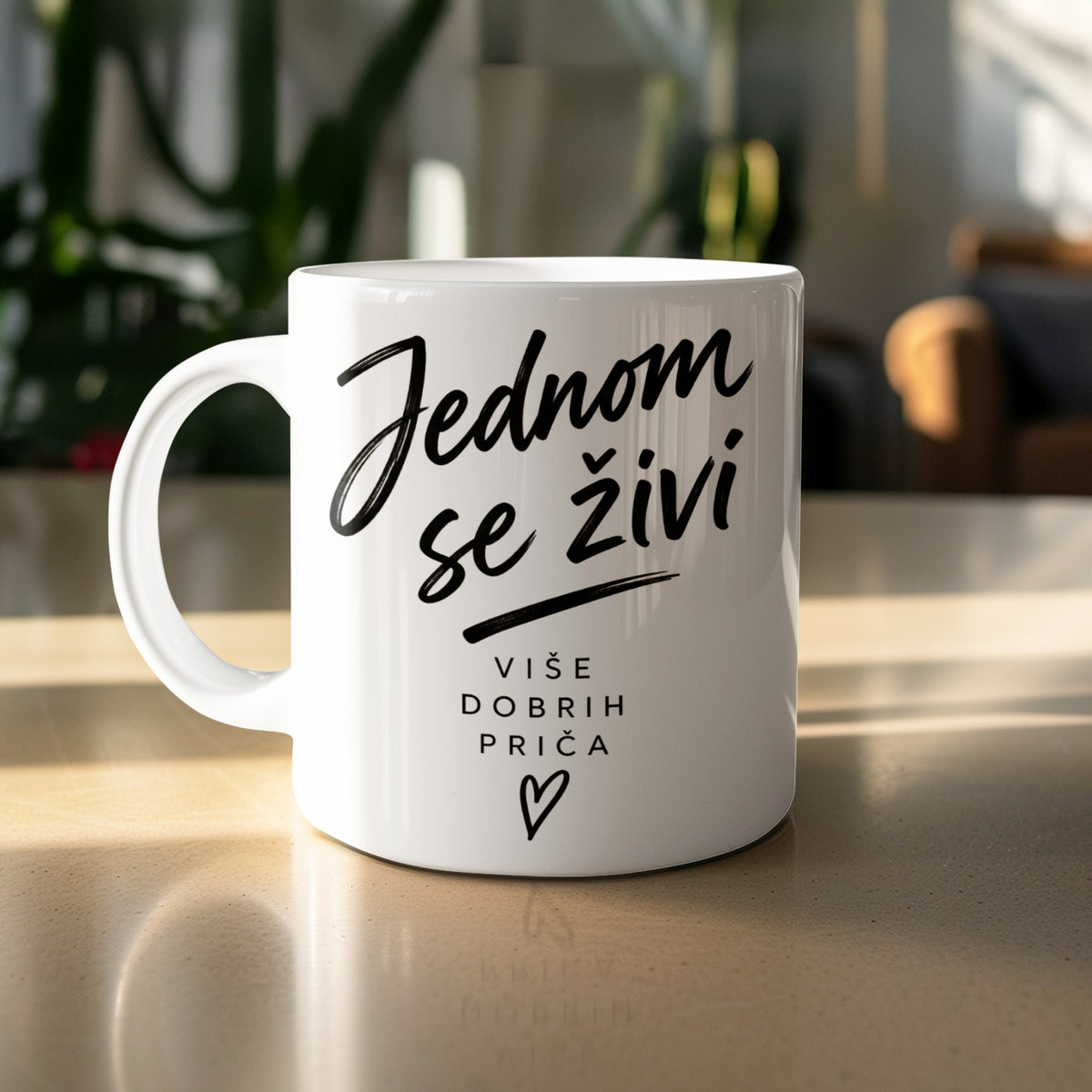 White mug with black text "Jednom se živi" and "Više dobrih priča" and a heart.