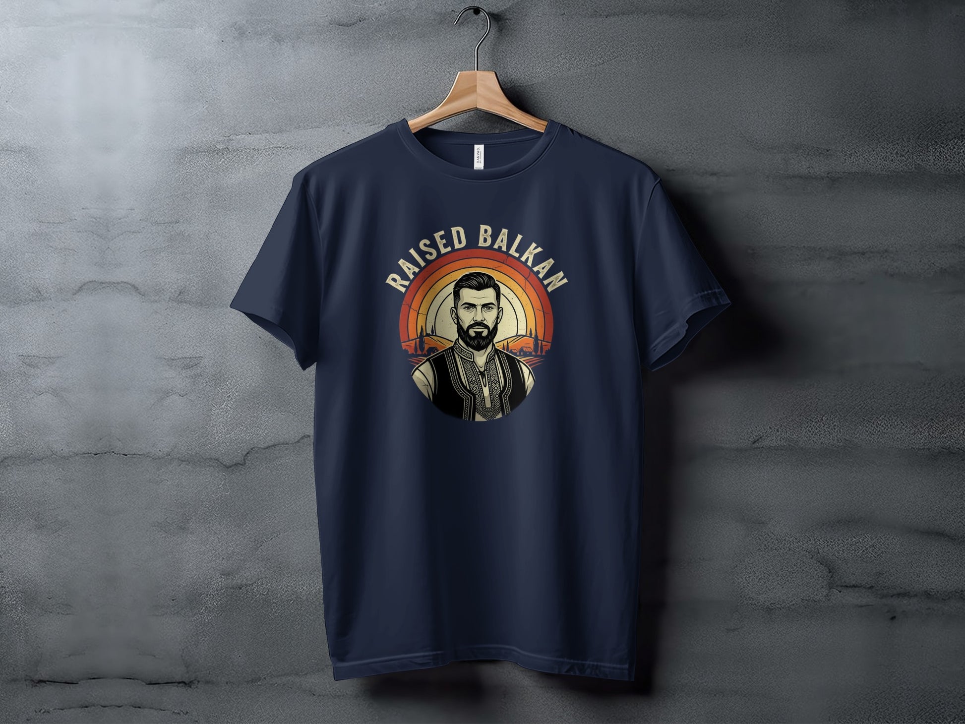 Navy t-shirt with "Raised Balkan" text and a portrait over a sunset landscape.