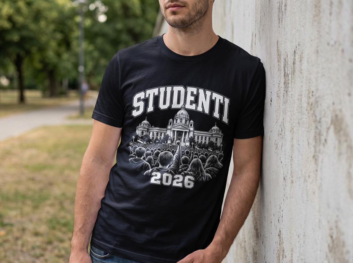 A man leaning against a concrete wall wearing a black t-shirt with a graphic of a crowd and building.