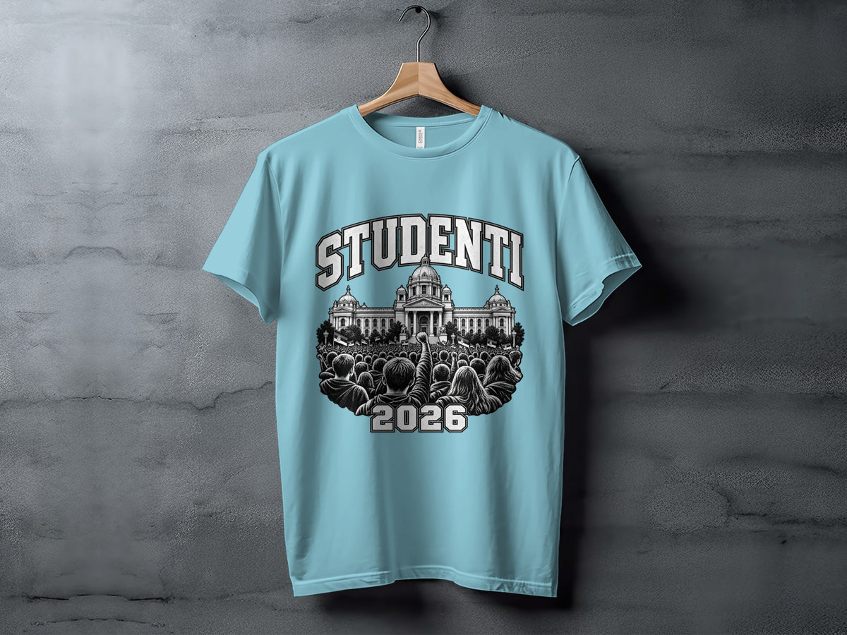 Light blue t-shirt hanging on a wooden hanger against a textured concrete wall, featuring a crowd illustration with the text "STUDENTI 2026".