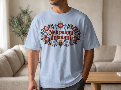 A man wearing a light blue t-shirt featuring a red floral graphic and the text Nek puknu dušmani.