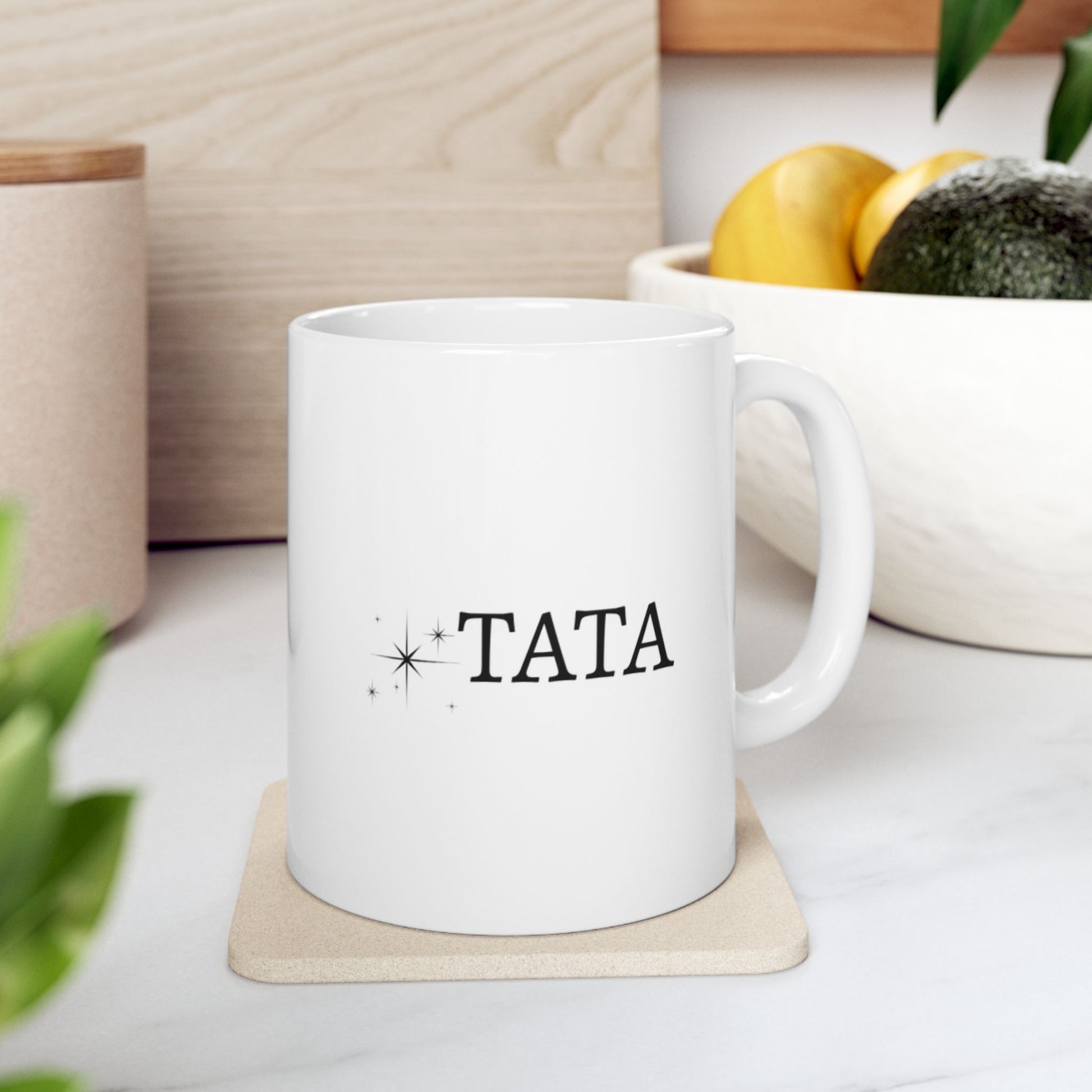 White mug with "TATA" and starburst design on a coaster.