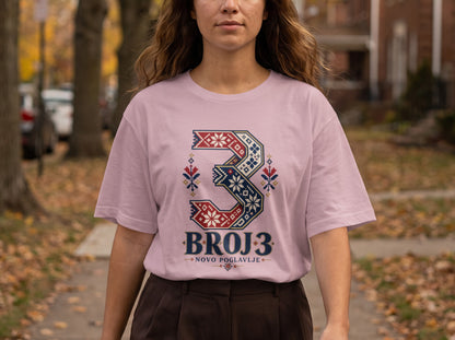 A woman wearing a pink t-shirt with a decorative number three and Serbian text.
