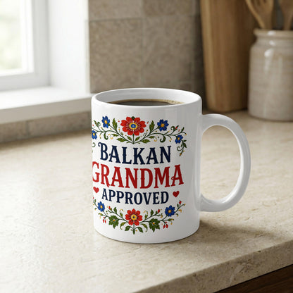 White mug with "Balkan Grandma Approved" and floral design.