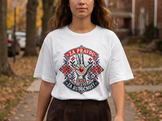 A woman wearing a white t-shirt featuring a stylized hand and text graphic with red, blue, and white folk embroidery patterns.
