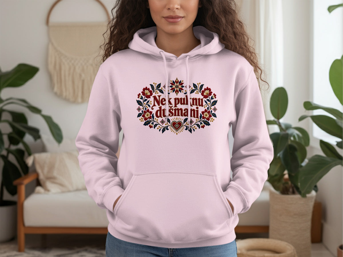 A person wearing a light pink hooded sweatshirt with red floral embroidery and text on the chest.