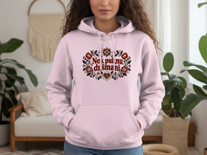A person wearing a light pink hooded sweatshirt with red floral embroidery and text on the chest.