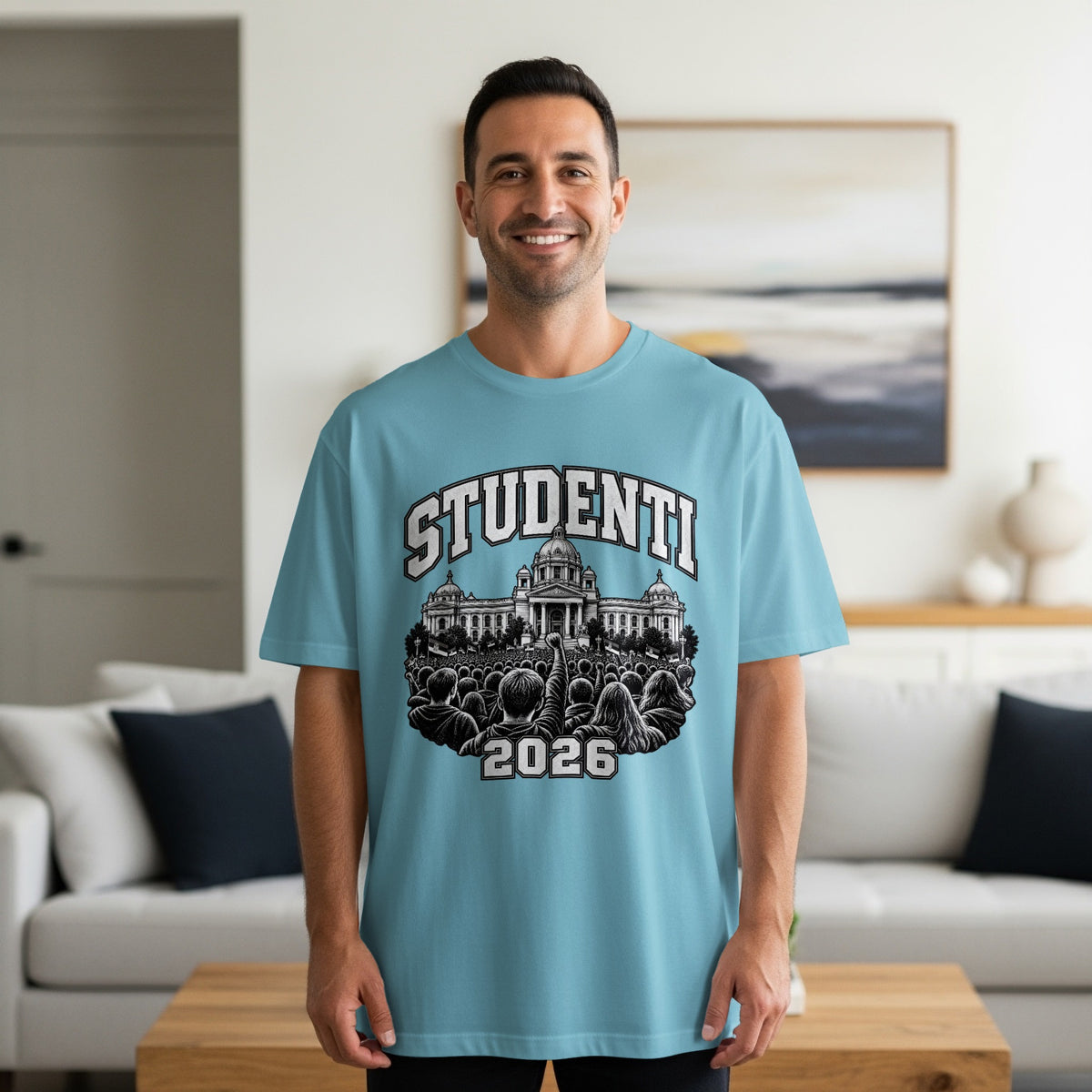 A smiling man wearing a light blue t-shirt with a graphic of a crowd and building.