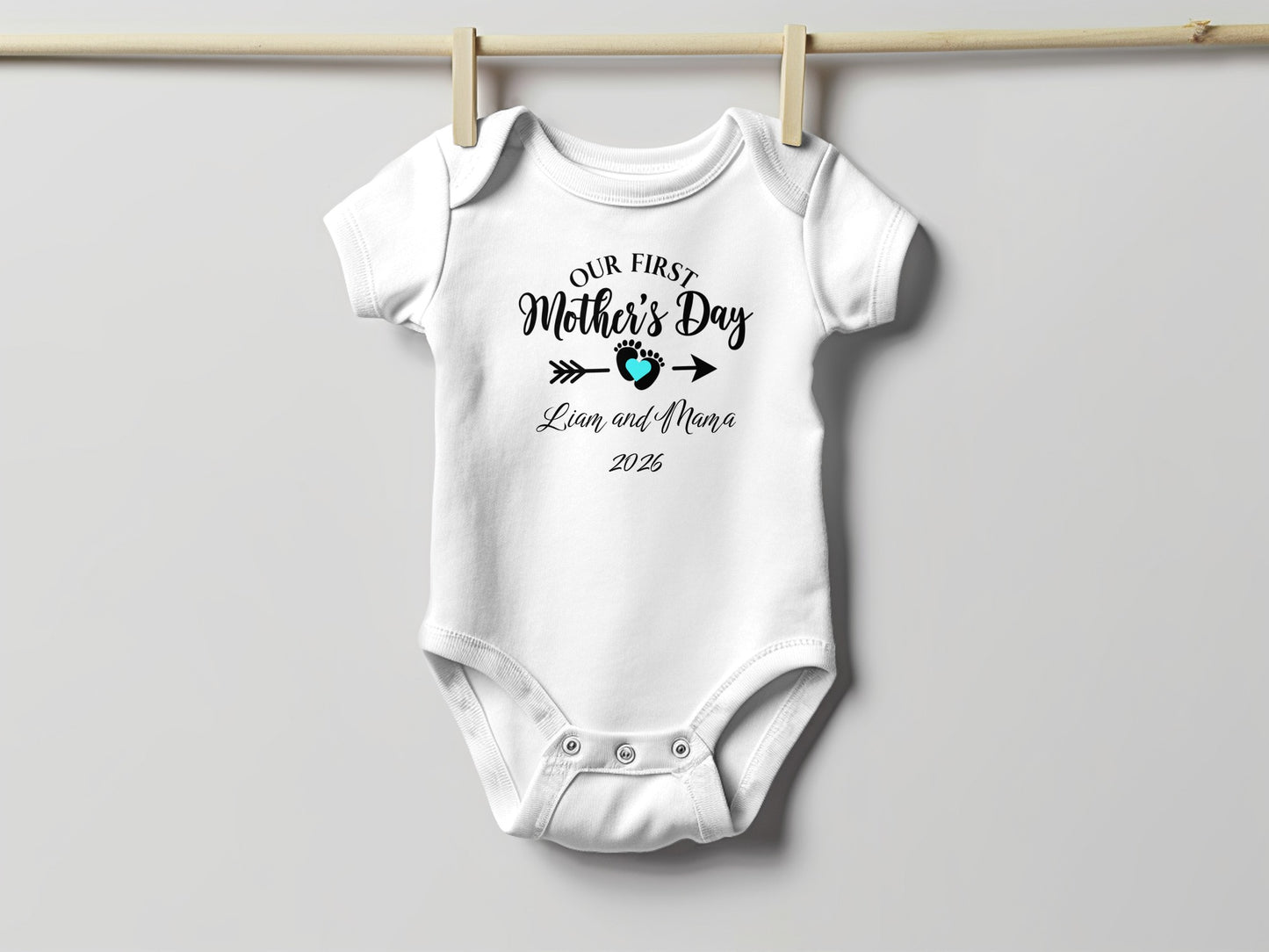 White baby onesie with "Our First Mother's Day" text and footprint.