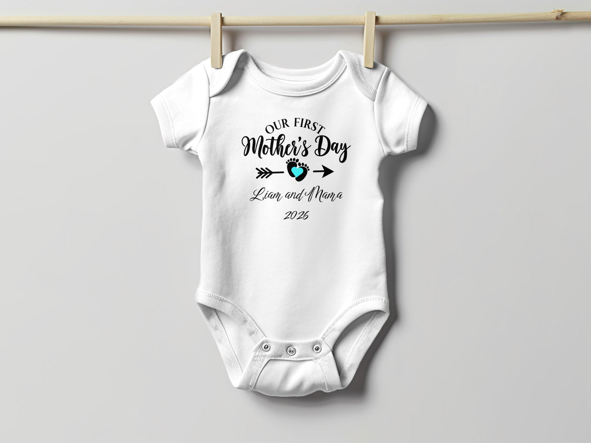 White baby onesie with "Our First Mother's Day" text and footprint.