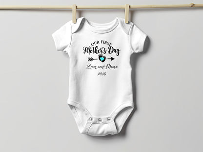 White baby onesie with "Our First Mother's Day" text and footprint.