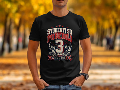 A man wears a black t-shirt featuring the text "STUDENTI SU POBEDILI 3 SRBIJA 2026".