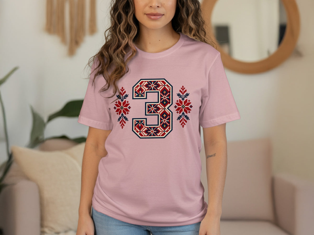 A person wearing a light pink t-shirt with a large number 3 printed in a red, blue, and white fair isle pattern.