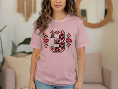 A person wearing a light pink t-shirt with a large number 3 printed in a red, blue, and white fair isle pattern.
