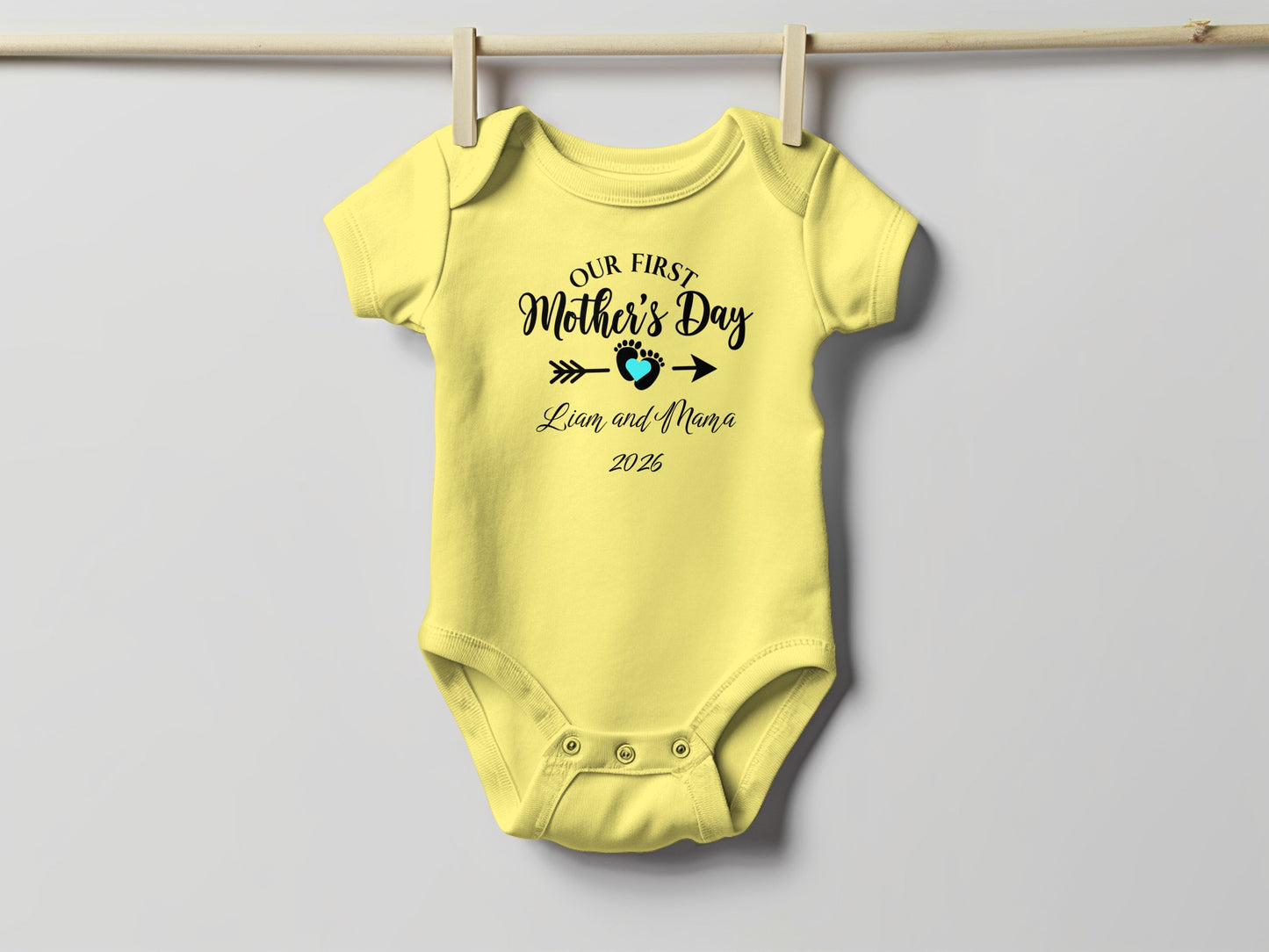 Yellow baby onesie with "Our First Mother's Day" text and a heart.