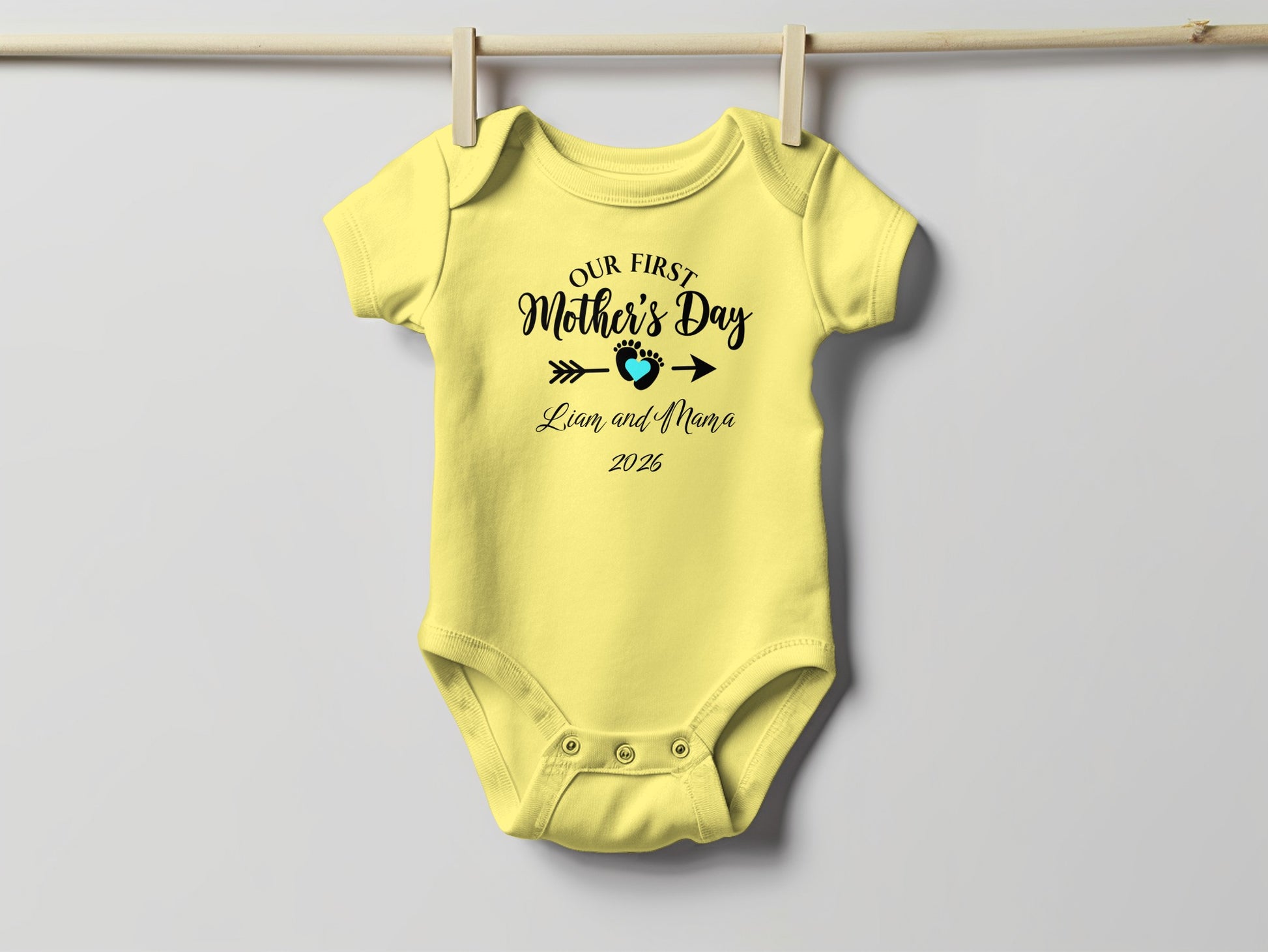 Yellow baby onesie with "Our First Mother's Day" text and a heart.
