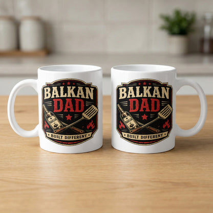 White mug with "BALKAN DAD BUILT DIFFERENT" text and grilling utensils.