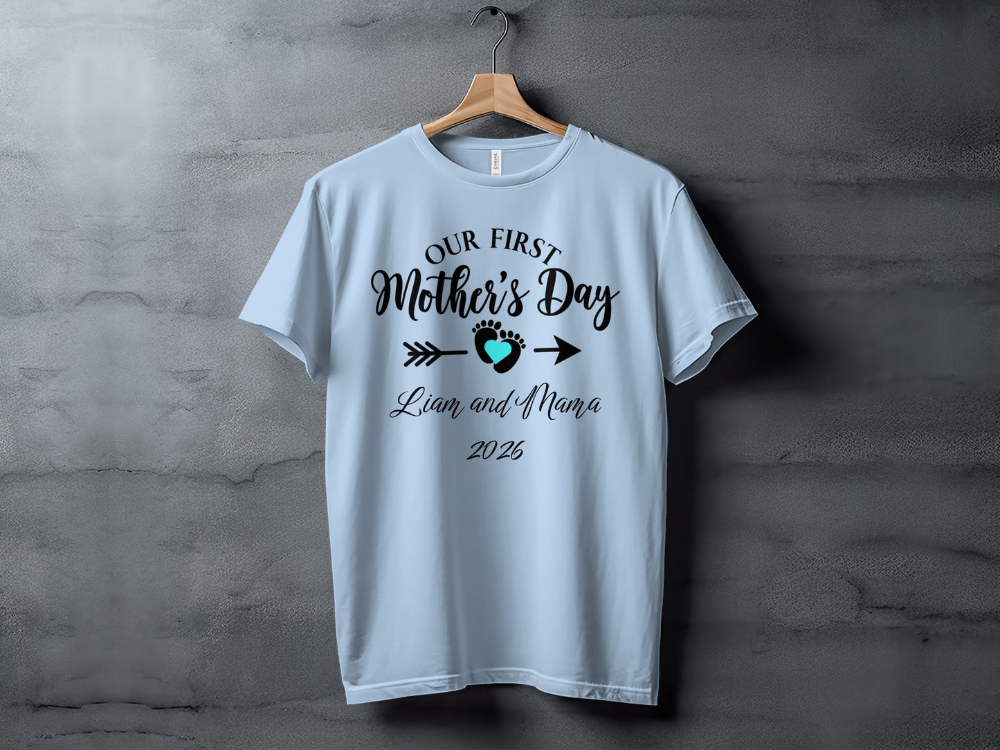 Light blue t-shirt with "Our First Mother's Day" text and heart arrow design.