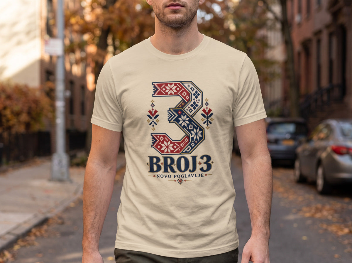 A man wearing a cream t-shirt featuring a stylized number three with folk patterns and the text BROJ 3.