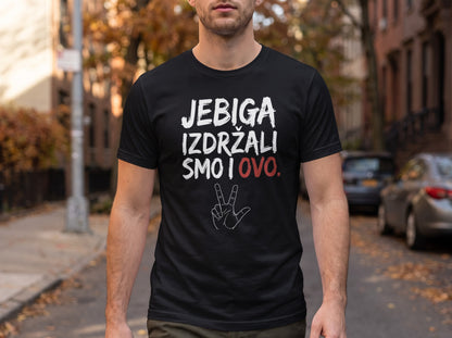 A man stands outdoors wearing a black t-shirt printed with white and red text, alongside a hand gesture.
