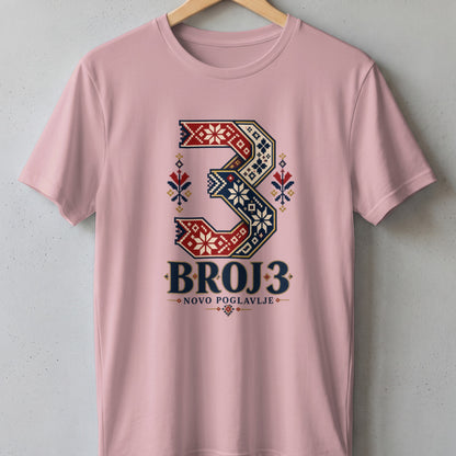 Pink short-sleeve t-shirt on a wooden hanger, featuring a large number three with traditional geometric embroidery patterns and the text BROJ 3 NOVO POGLAVLJE.